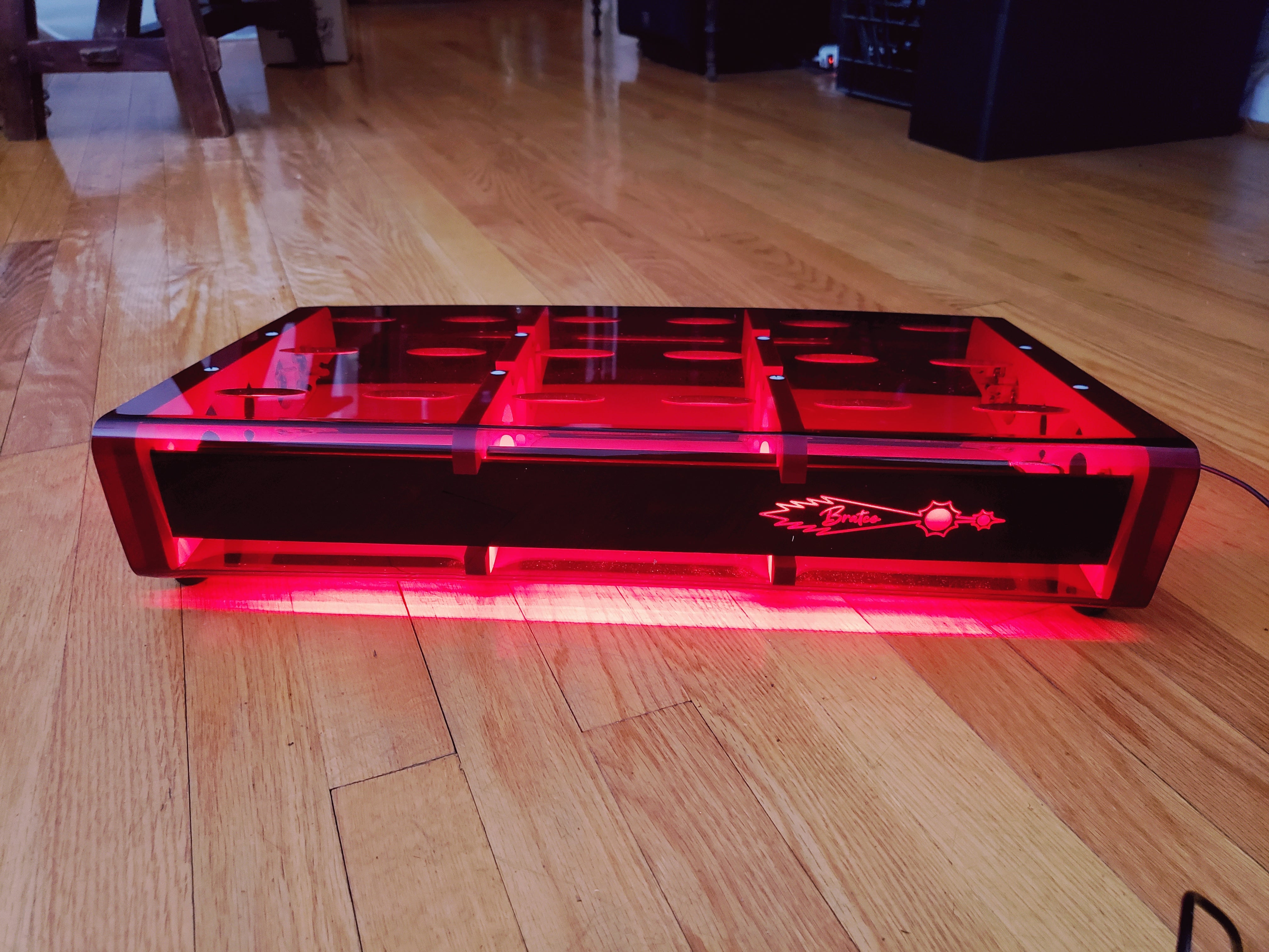 Red lit bratco innovations bass pedal board, front view, daylight on wood floor